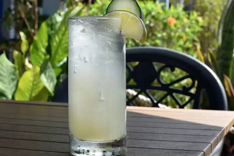 Cold iced drink with lime and cucumber slices outdoors.