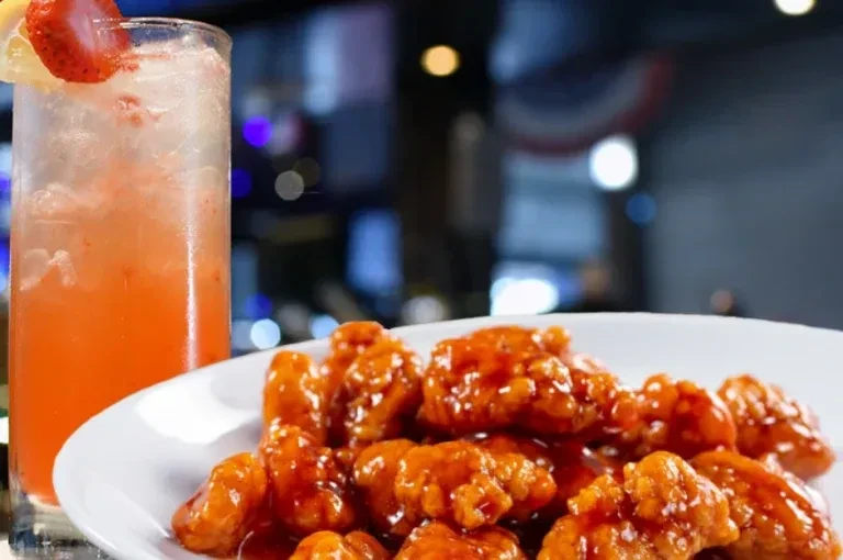 Glistening chicken wings with orange sauce next to a strawberry cocktail.
