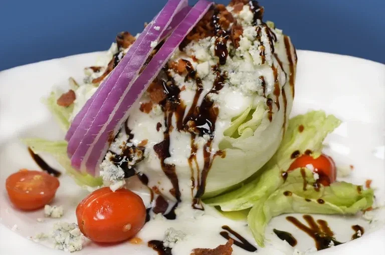 Plated wedge salad with blue cheese, bacon, red onion, and balsamic glaze.