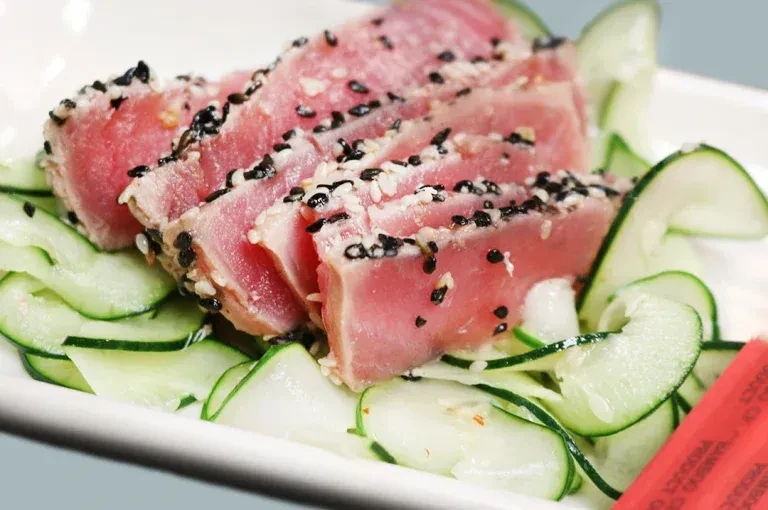 Pink seared tuna tataki with sesame seeds on cucumber ribbons.