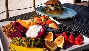 Rectangular platter of colorful fresh fruits, yogurt, and granola outdoors.