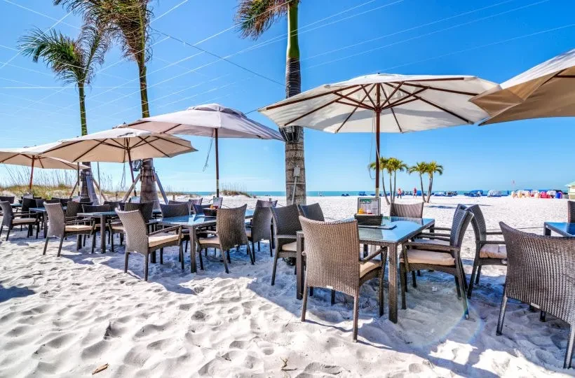 Outdoor dining on a white sandy beach with palm trees and ocean.