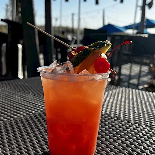 Iced, layered orange-red drink with fruit skewer on outdoor table.