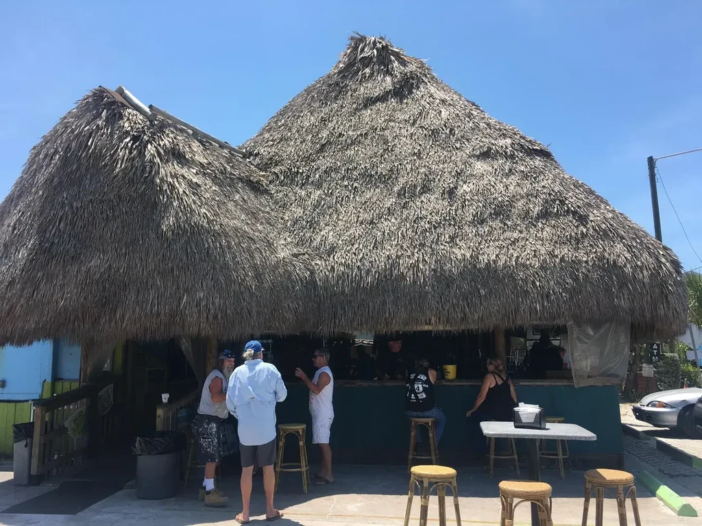 People at a vibrant open-air bar with a thatched roof.