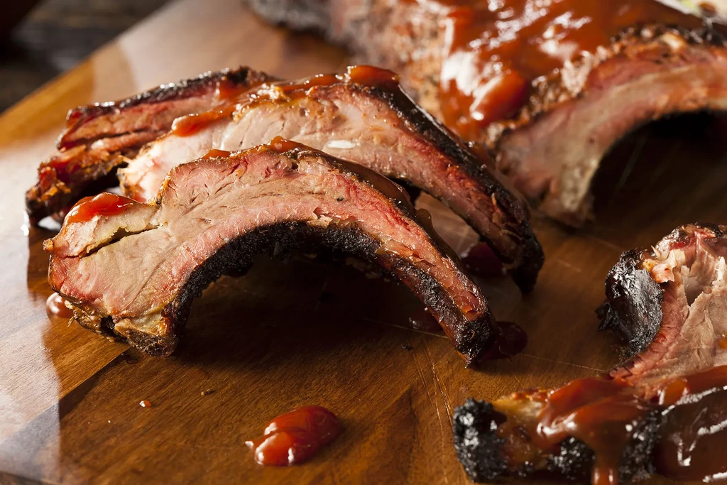 Sliced, charred barbecue ribs with smoke ring and sauce on wood.