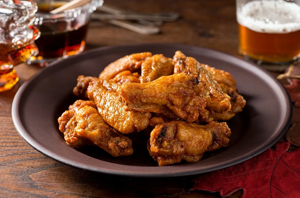 Crispy golden chicken wings, dipping sauce, and beer on a rustic table.