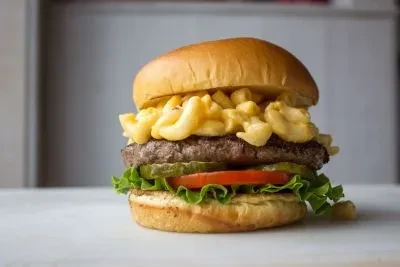 Gourmet burger on brioche with macaroni and cheese, patty, and vegetables.