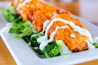 Fried chicken tenders with buffalo sauce, white drizzle, and lettuce.