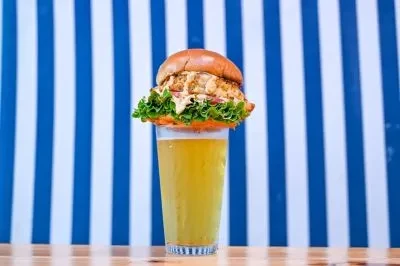 Burger with lettuce on cold beer glass, blue striped background.