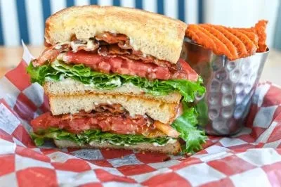 Close-up: Stacked BLT club sandwich, waffle sweet potato fries on checkered paper.