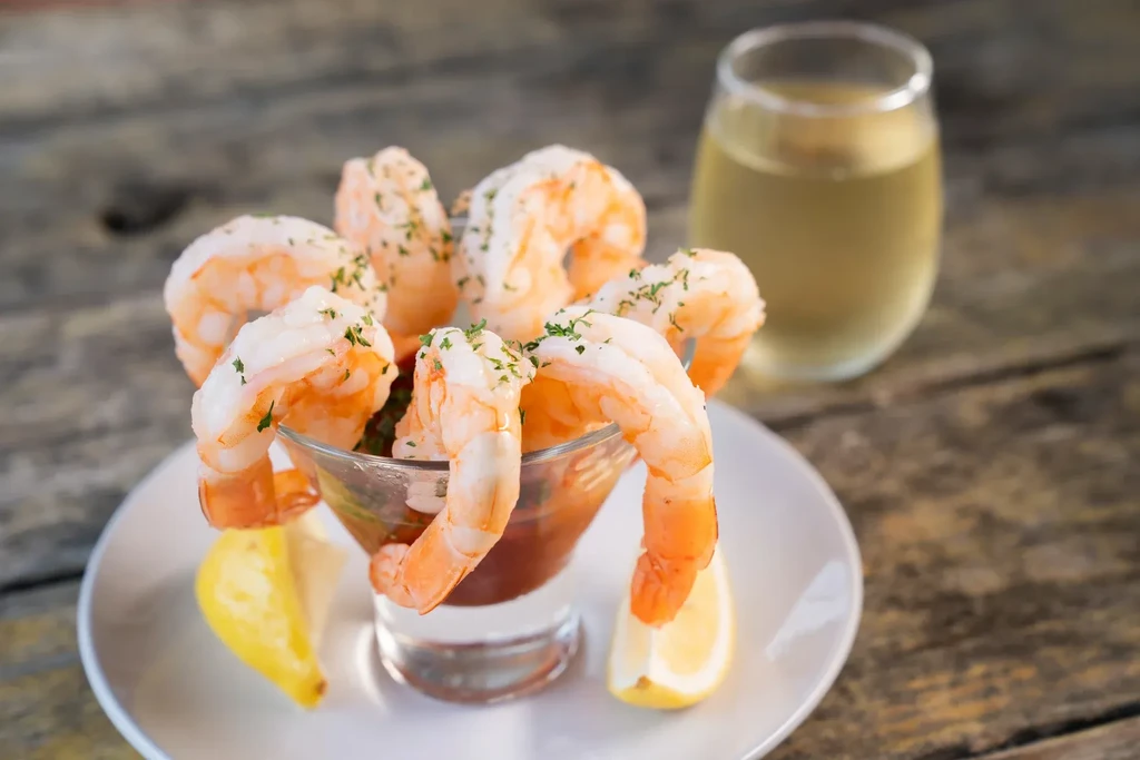 Shrimp cocktail with lemon, herbs, and wine on a rustic wooden table.