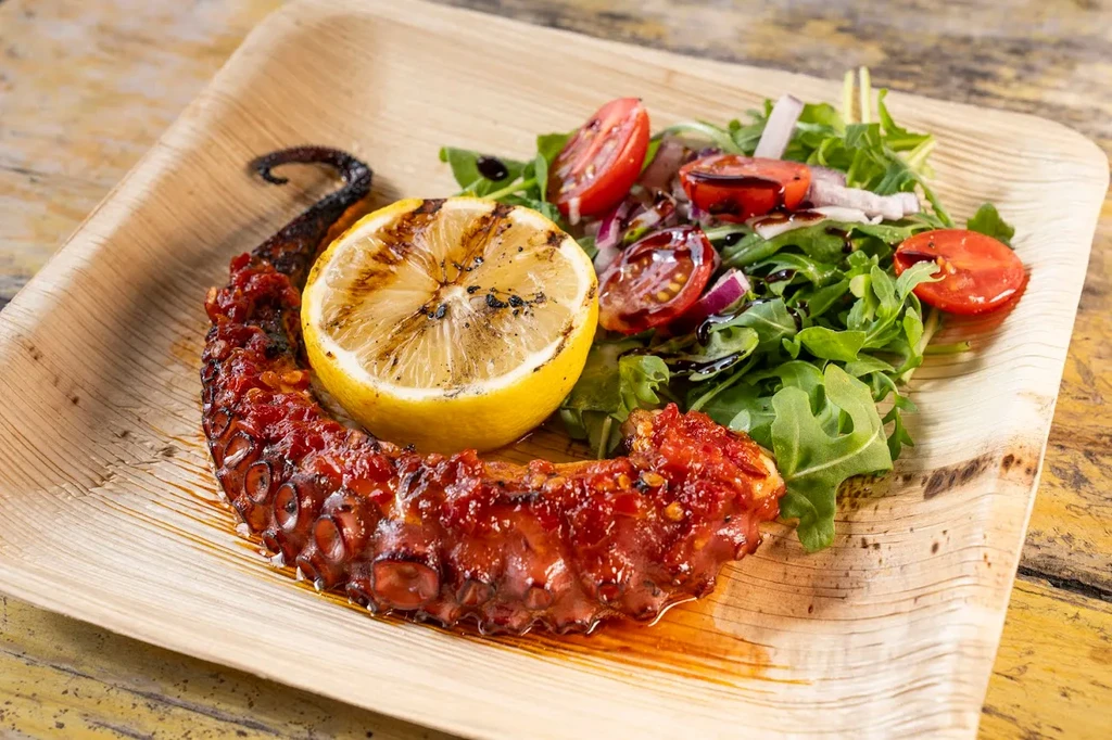 Grilled octopus, charred lemon, and fresh salad on a natural plate.