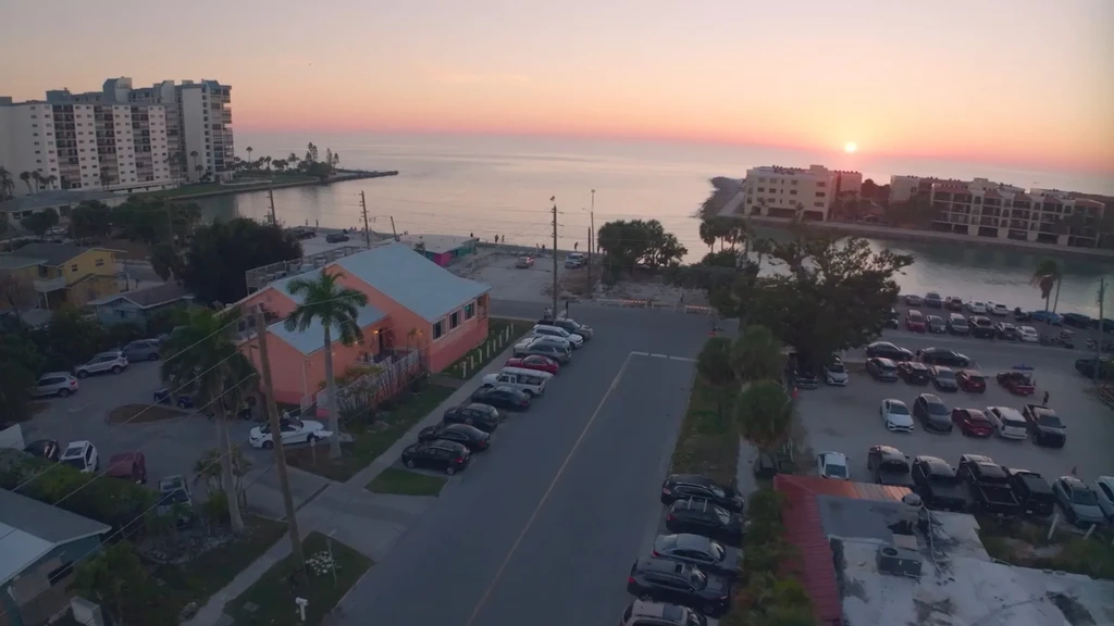 Aerial photo: coastal urban scene at golden hour, colorful sky, cars.