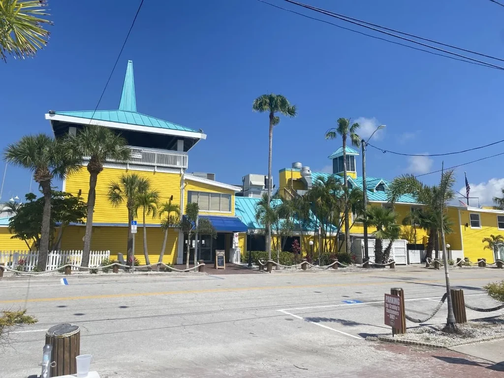 Bright yellow Crabby's building with turquoise roofs, tower, and palm trees.