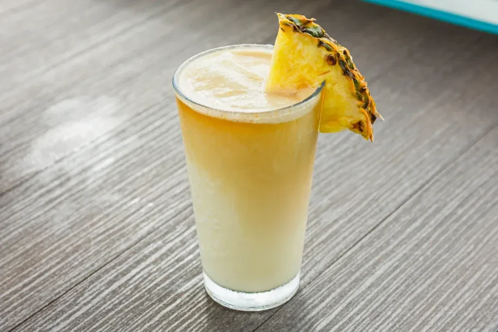 Tall glass with frothy gradient drink, garnished with a pineapple wedge.