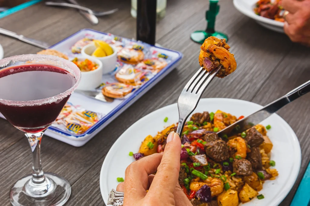 Hand forking shrimp from colorful meal next to red martini.