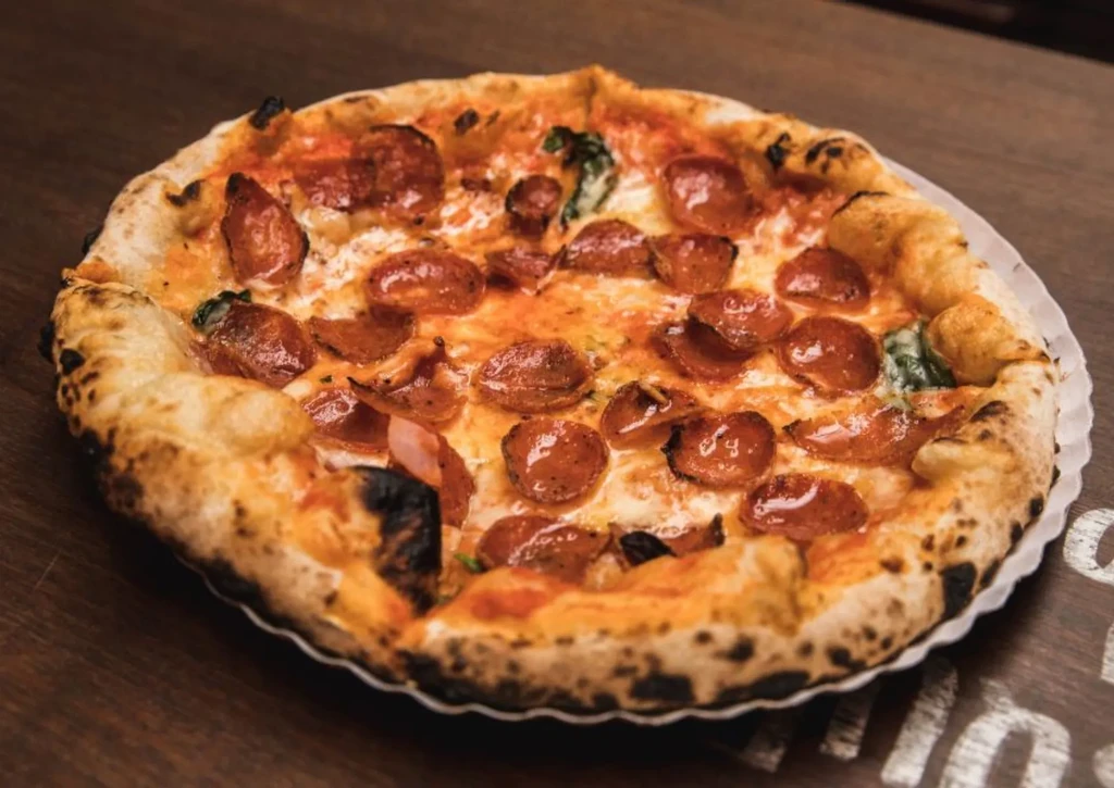 Close-up of wood-fired pepperoni pizza with melted cheese and bubbling crust.