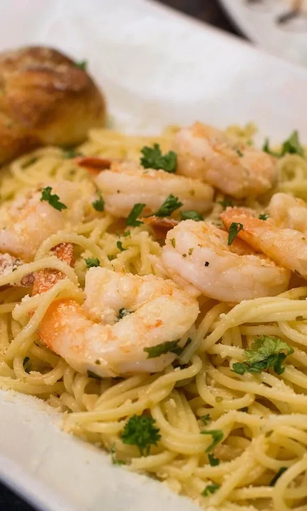 Close-up of spaghetti with shrimp, light sauce, herbs, and cheese.