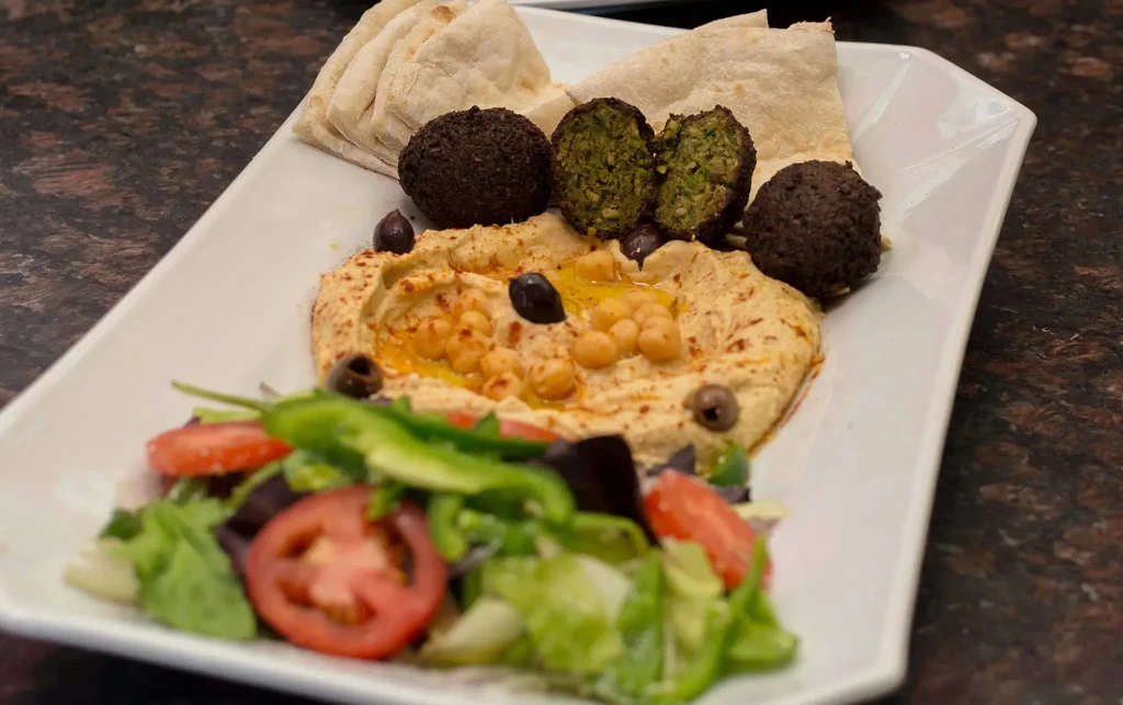 Hummus with falafel, pita bread, and salad on a white plate.