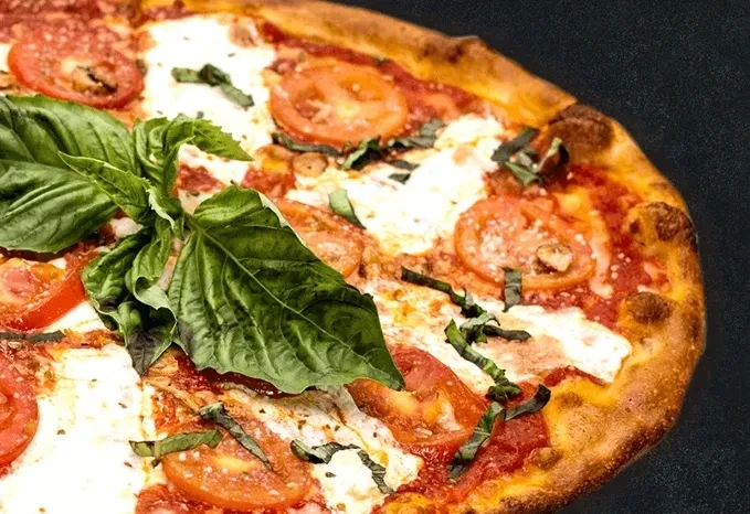 Margherita pizza with golden crust, red tomatoes, white mozzarella, green basil.