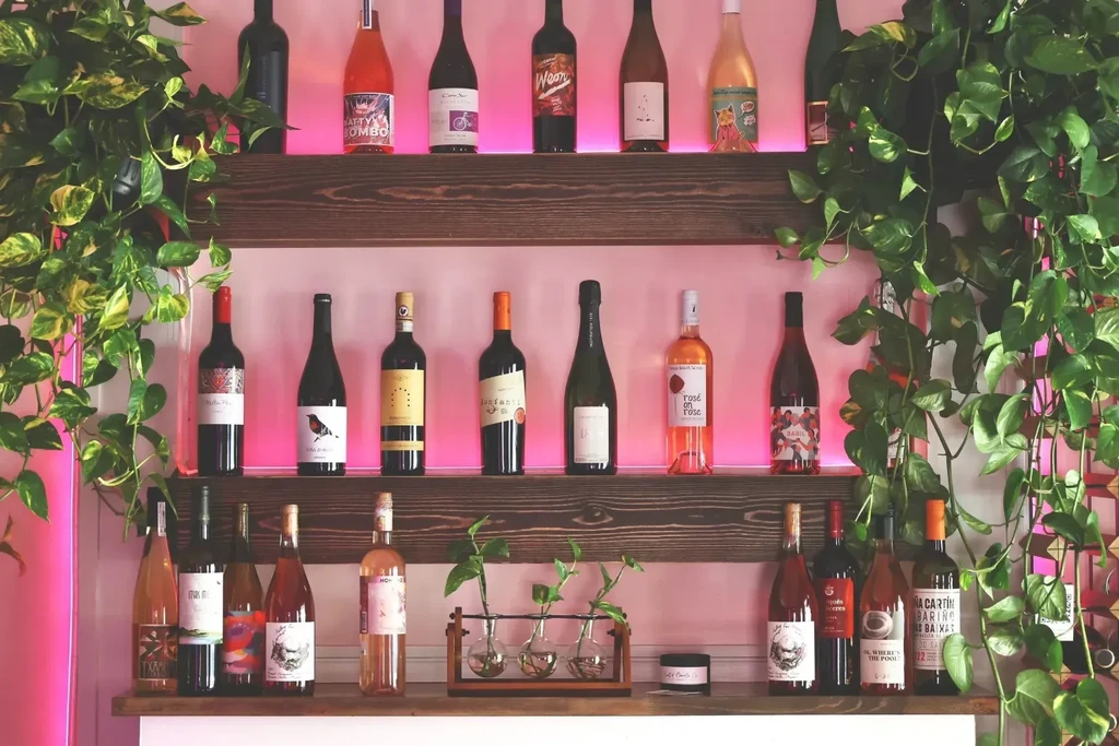 Wooden wall shelves with wine bottles, cascading plants, and pink LED glow.