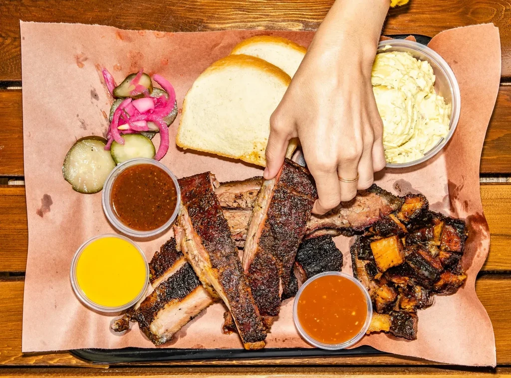 A hand grabs ribs from an overhead BBQ platter with sides.