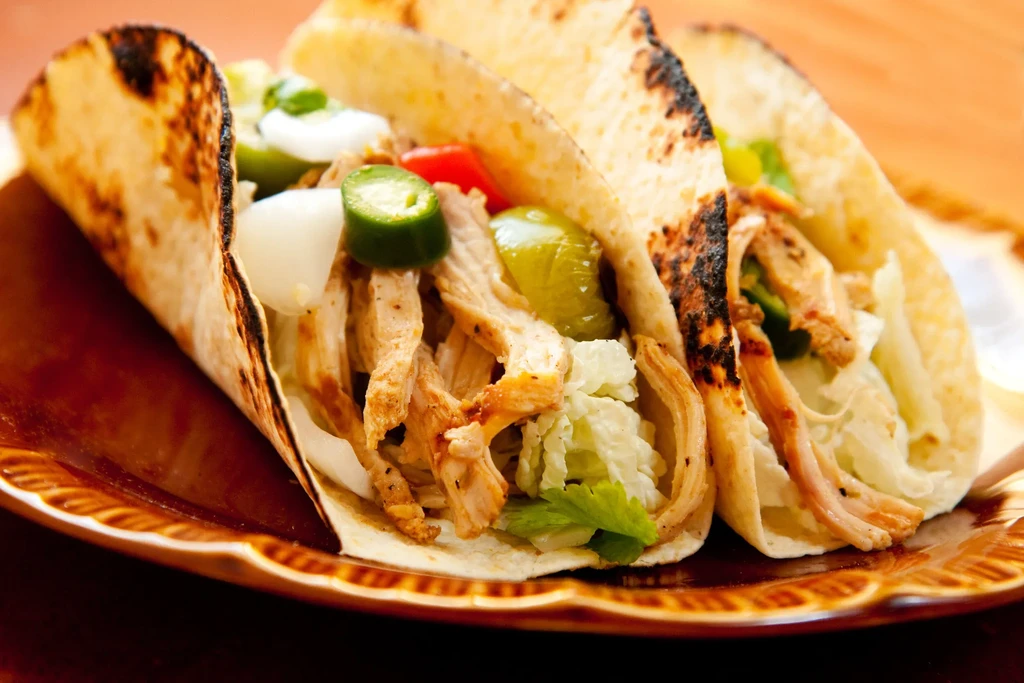 Three grilled soft-shell tacos with shredded meat, lettuce, onions, and peppers.