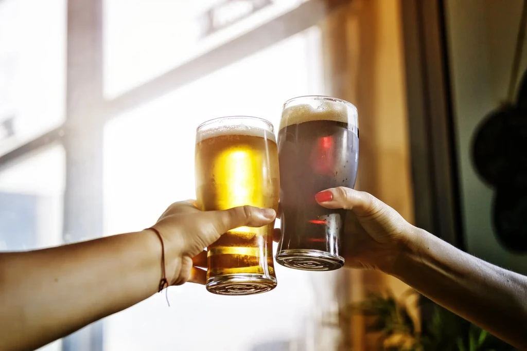 Two hands toast with glasses of light and dark beer.