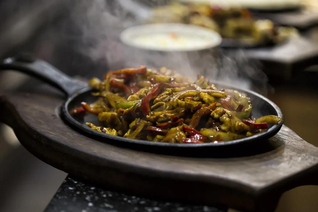 Sizzling meat and colorful vegetables in a cast-iron skillet.