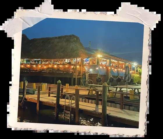 Thatched-roof restaurant on the water, lit by string lights at dusk.