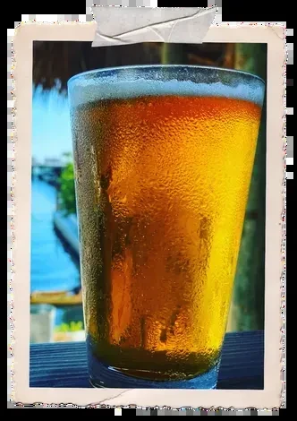 Sweating glass with golden-amber drink and foam, waterside setting.