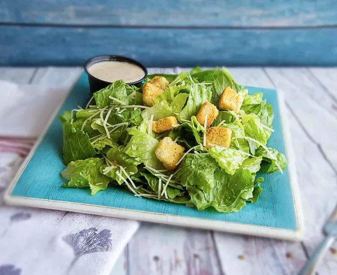 Vibrant Caesar salad with Parmesan, croutons, and dressing on a teal plate.