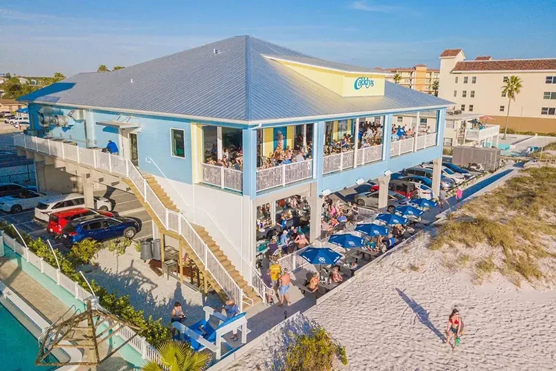 Aerial view: multi-story beach restaurant with patrons on a sunny day.