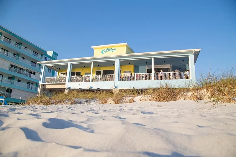 Colorful Caddy's restaurant building on a sandy beach under blue sky.