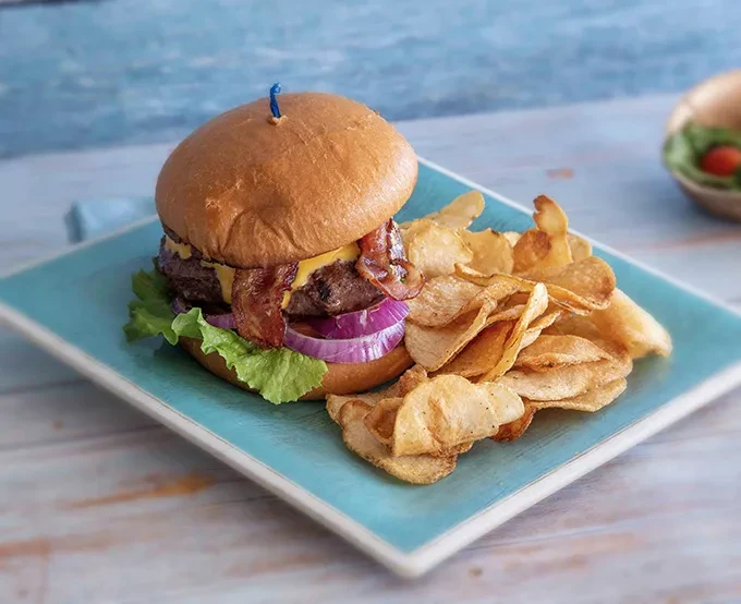 Bacon cheeseburger with potato chips on a teal-blue plate.