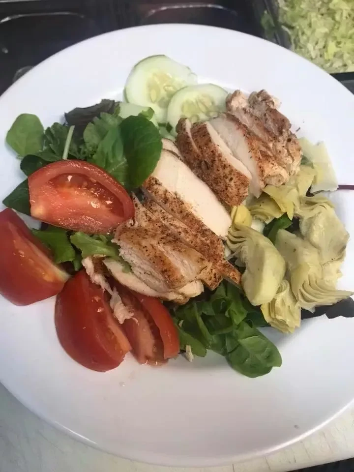 Grilled chicken salad with greens, tomato, cucumber, and artichoke hearts.