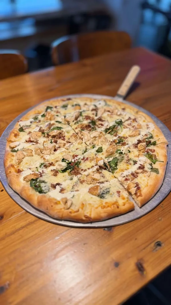 Sliced white sauce pizza with chicken, bacon, spinach, and ranch drizzle.