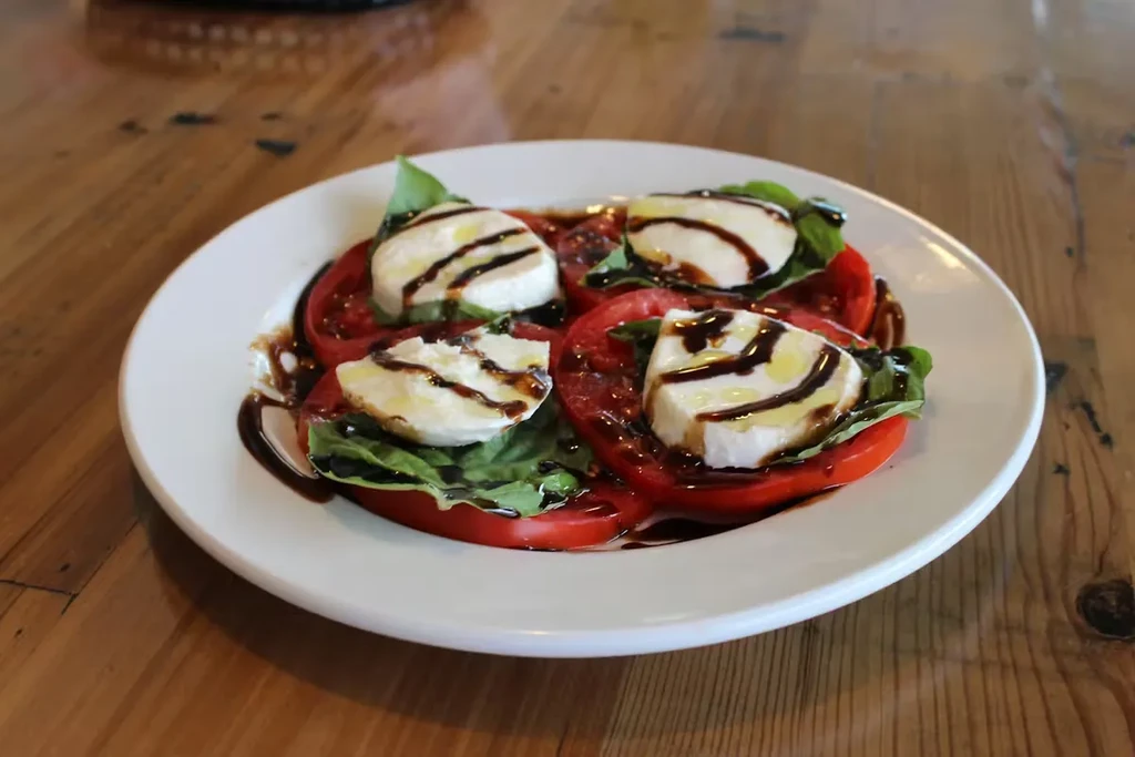 Close-up of Caprese salad with tomato, mozzarella, basil, balsamic drizzle.