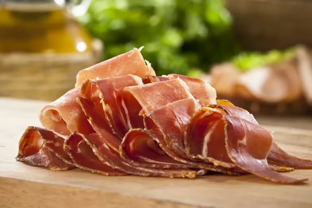 Generous pile of thinly sliced cured meat on a wooden board.