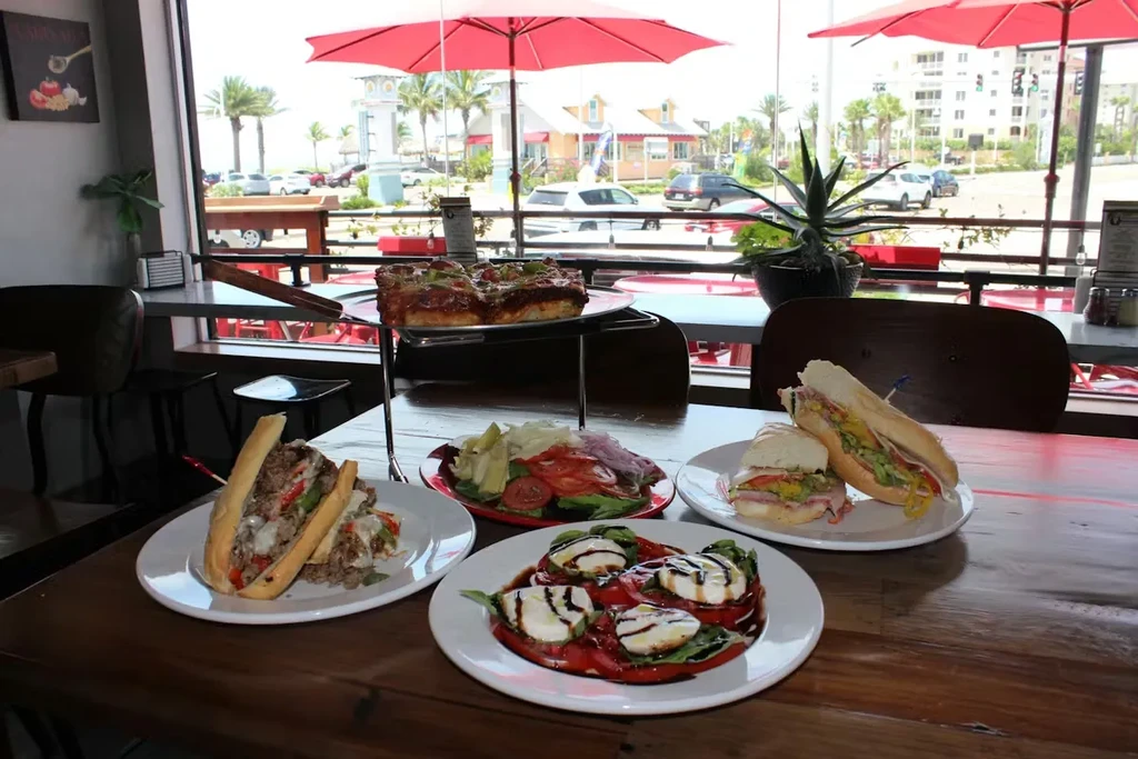 Restaurant table with sandwiches, salads, pizza, and a sunny outdoor view.
