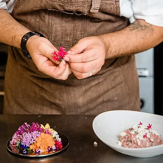 Chef's hands meticulously arranging edible flowers on a dish.