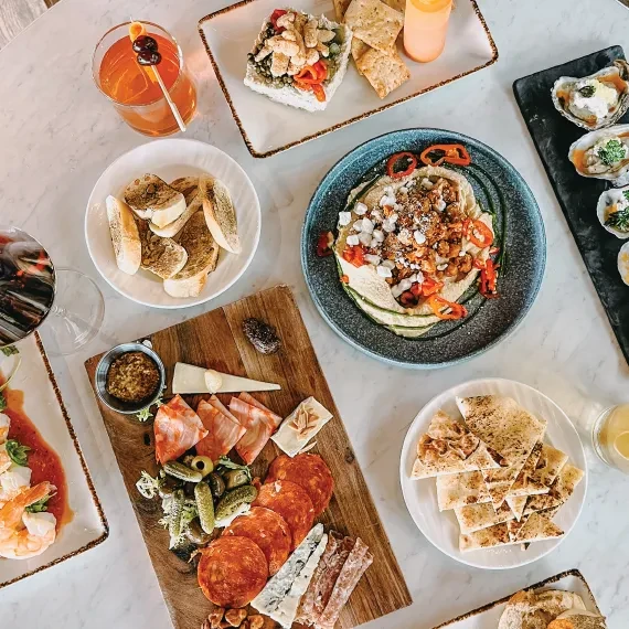 Overhead view of a table with diverse appetizers, charcuterie, seafood, and drinks.