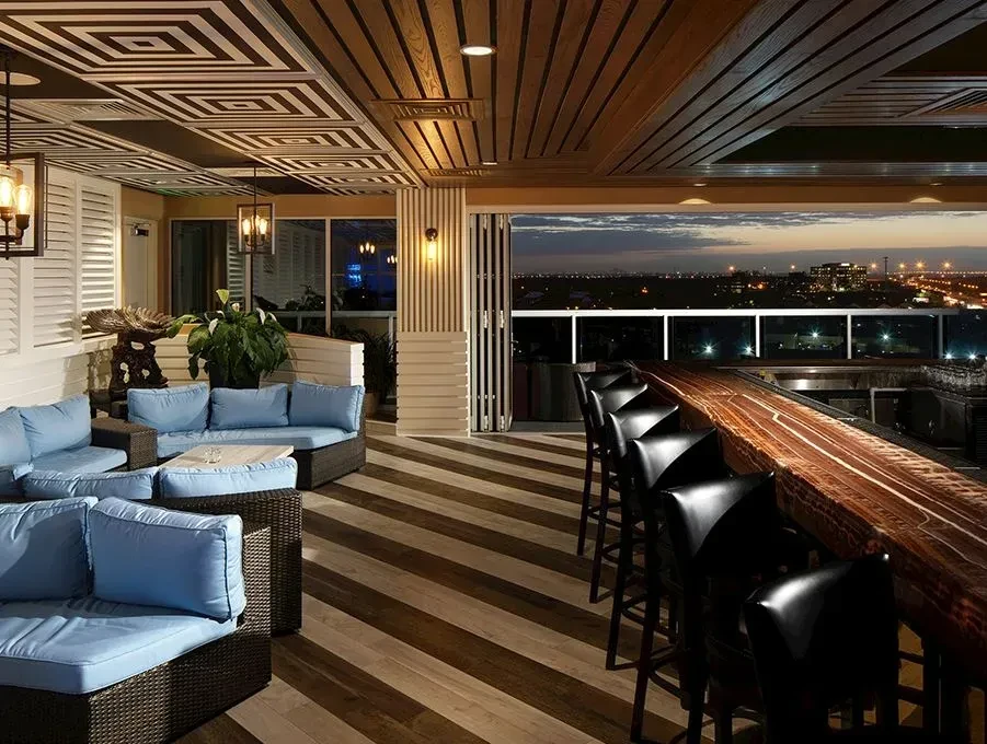 Modern rooftop bar, sofas, wooden bar, panoramic city view at dusk.