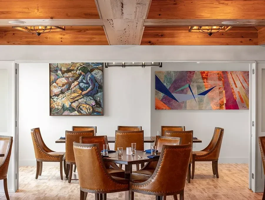 Well-lit dining area with square table, eight leather chairs, two artworks.