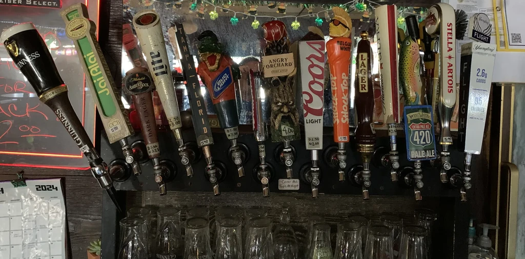 Many beer tap handles with pint glasses and green shamrock lights.