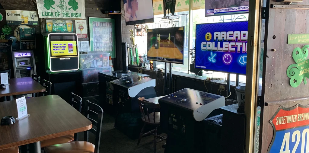 A casual bar interior with arcade games, multiple TVs, and Irish flag.