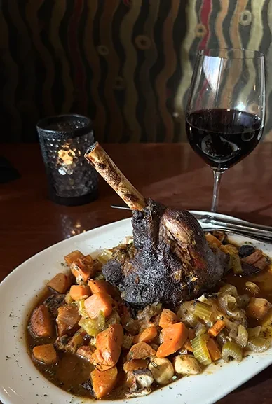 Lamb shank, braised vegetables, red wine, and a glowing candle.
