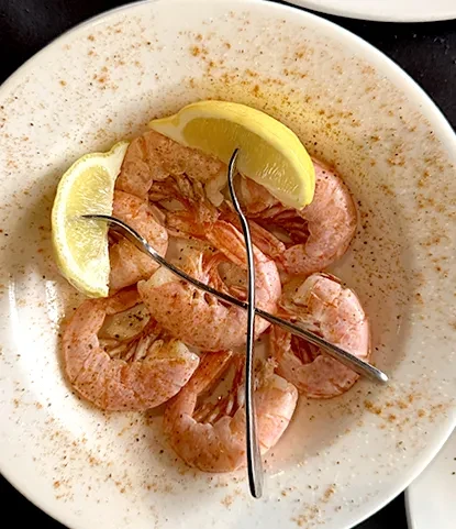 Five seasoned shrimp with lemon and forks on a speckled plate.