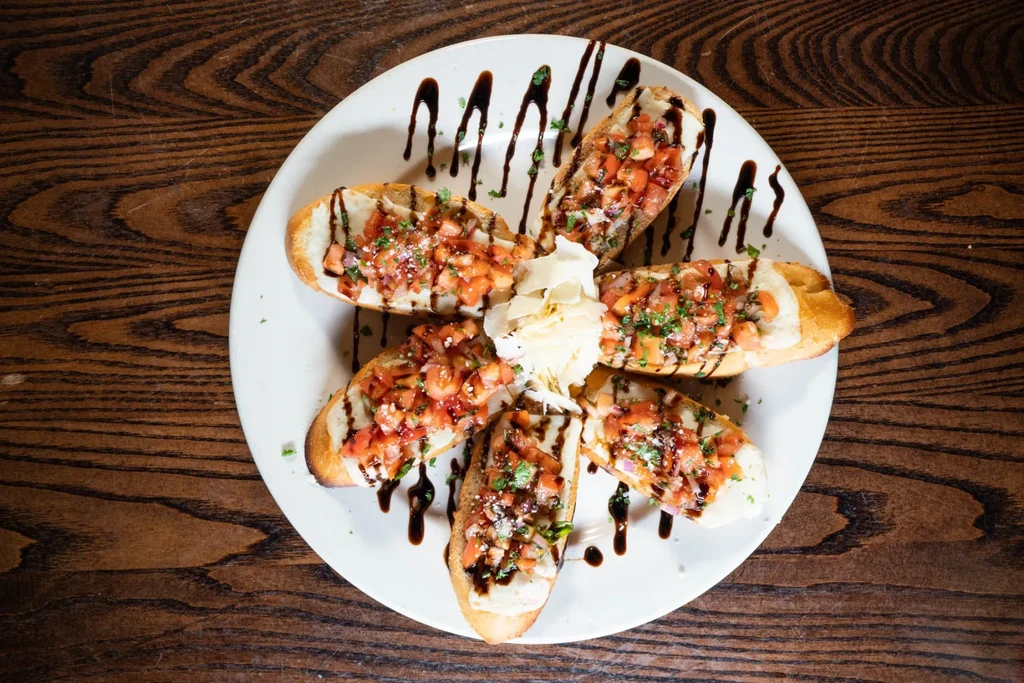 Plate of six bruschetta with tomatoes, herbs, balsamic, and cheese.