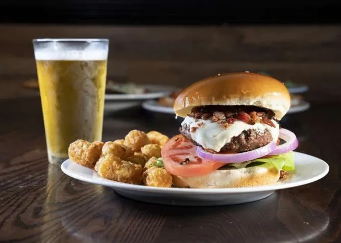 Gourmet burger, tater tots, and beer served on a wooden table.